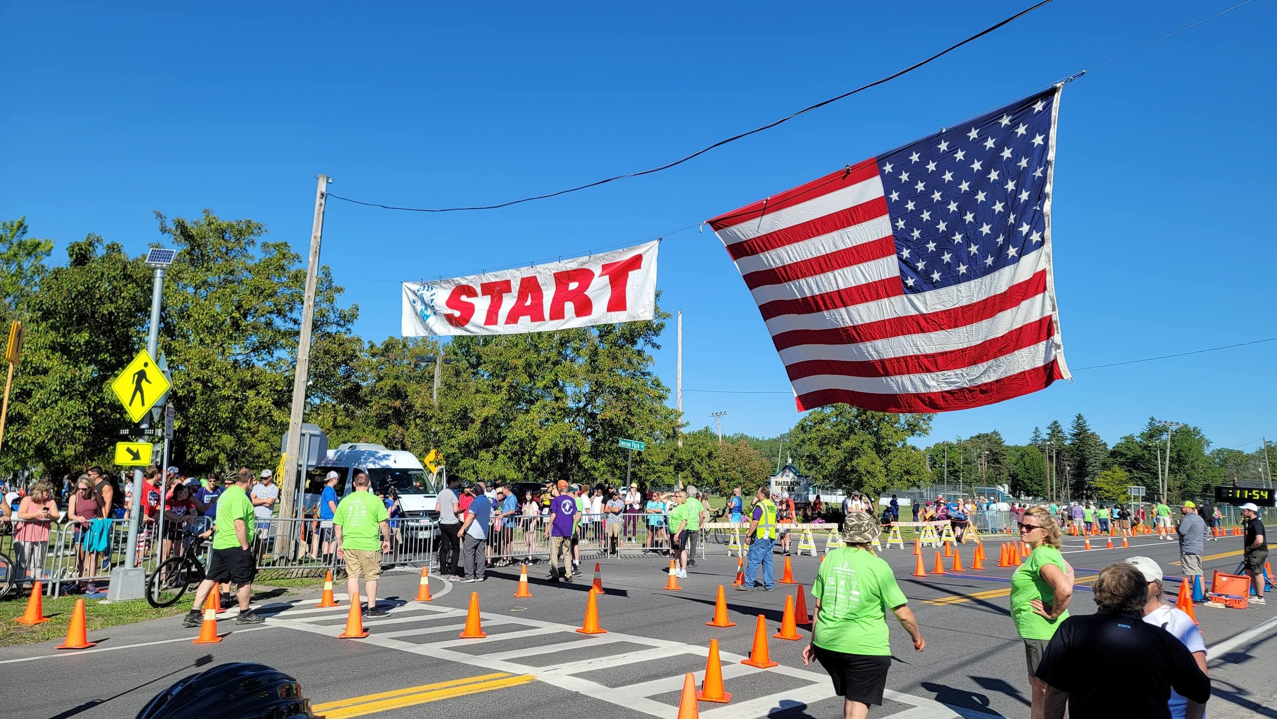 The Great Race start area before the race: an American flag billows next to the START banner above safety cones laid out across the road.